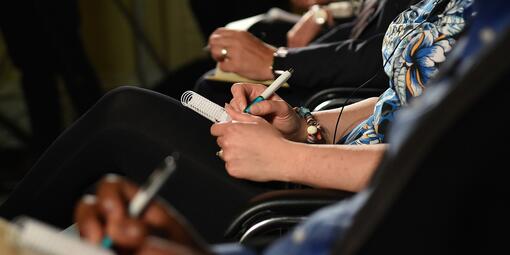 In einer Reihe sitzen Personen. Sie schreiben in ein Notizbuch.