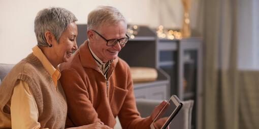 Ein älteres Paar sitzt auf dem Sofa und schaut gemeinsam auf ein Tablet.