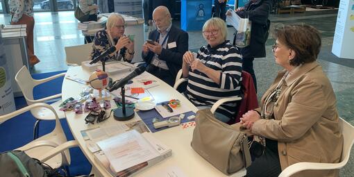 Personen tauschen sich am Tisch zum Thema Sehbehinderung aus. Auf dem Tisch liegen einige Materialien, beispielsweise ein Modell des Auges und Infobroschüren. 