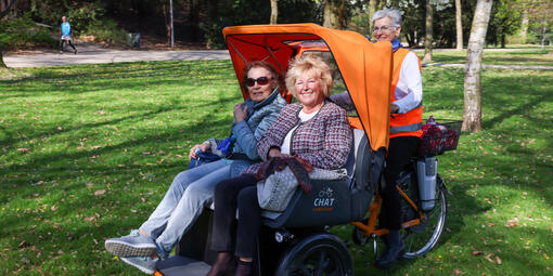 Zwei Frauen sitzen in einer Rikscha, die von einer weiteren Frau gefahren wird.