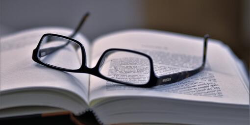 Eine Brille liegt auf einem aufgeschlagenen Buch. 