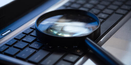 Eine Lupe liegt auf der Tastatur eines Laptops. 