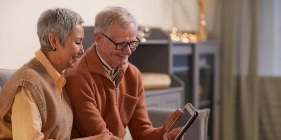 Ein älteres Paar sitzt auf dem Sofa und schaut gemeinsam auf ein Tablet.