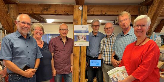 Fotographie von sechs Menschen um die 60 Jahre, die in einem Halbkreis stehen