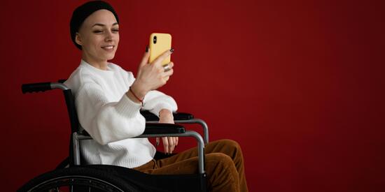 Eine junge Frau sitzt in einem Rollstuhl. Sie nutzt ein Handy.