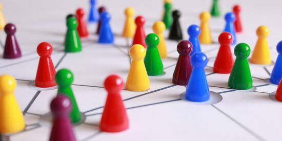 Kleine Spielfiguren in vielen verschiedenen Farben stehen auf einem Spielbrett. Das Spielbrett hat Linien, durch die die einzelnen Figuren miteinander verbunden sind. 