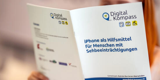 Eine junge Frau liest den Leitfaden des Digital-Kompass "iPhone als Hilfsmittel für Menschen mit Sehbeeinträchtigung".