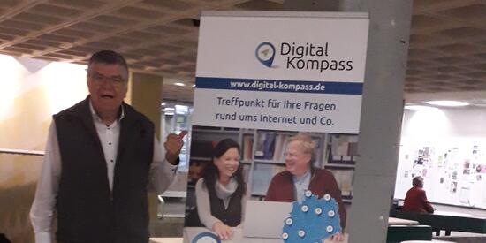 Siegbert Schlor steht neben dem Aufsteller des Digital-Kompass. Darauf steht "www.digital-kompass.de - Treffpunkt für Ihre Fragen rund ums Internet und Co."